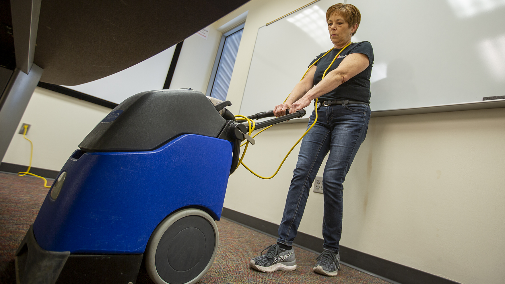 Nebraska's Tracy Oehlerking cleans the carpet below a desk in a Schorr Center meeting room on March 25, 2022. After careers in cosmetology and real estate, Oehlerking found her passion helping keep campus spaces clean for students, faculty and staff.