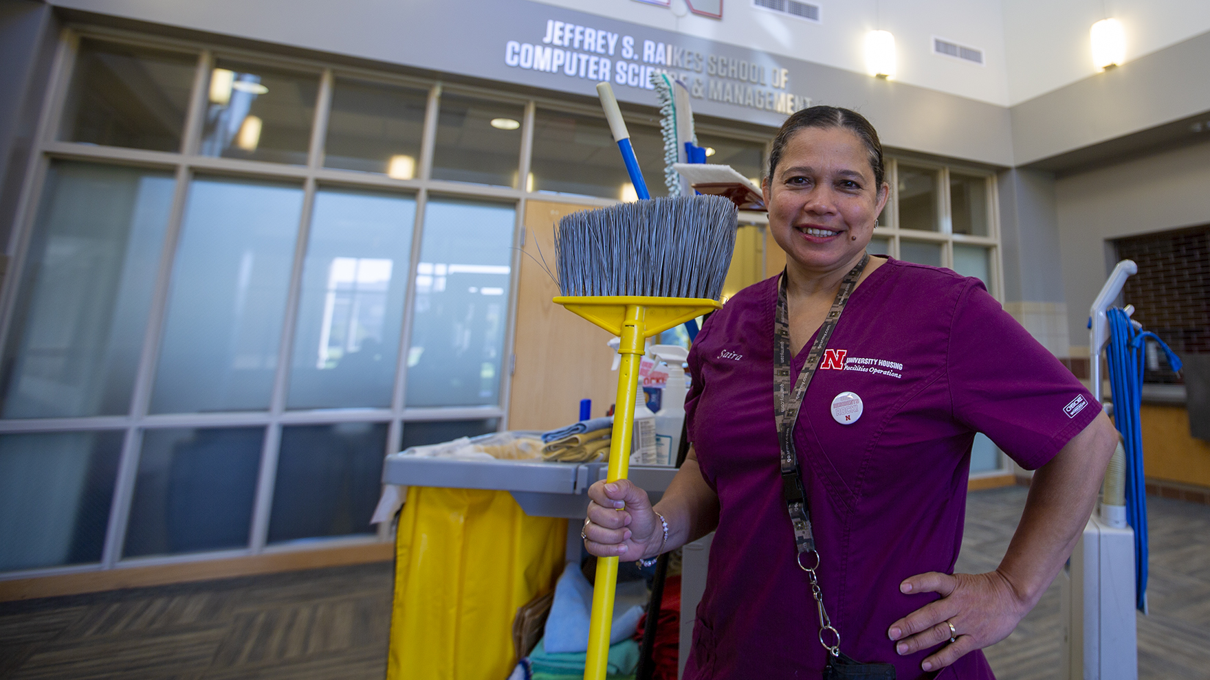 Nebraska's Saira Bautista de Preciado stands proudly, holding a broom, in Kauffman Hall. Bautista de Preciado has worked as a custodian in the Raikes School for 10 years and recently received an Employee Service Award for her dedication to the university.