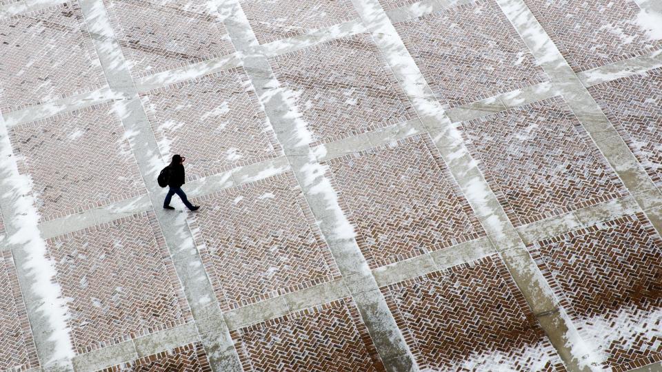 A student walks across the brick plaza outside of East Memorial Stadium.
